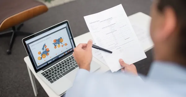 Professional setting with businessman reviewing documents and data on a laptop in an office. a man holding an application form