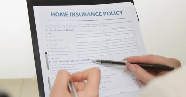 Hands holding pens filling out a home insurance policy document for coverage details. a home insurance policy