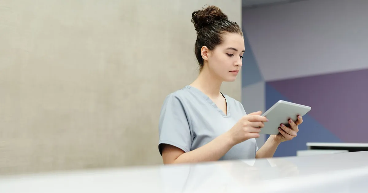 A receptionist in scrubs using a tablet at an office reception desk. a receptionist looking at a tablet