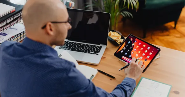 A man using a tablet and laptop at a desk in a modern office setting. a man using a digital tablet