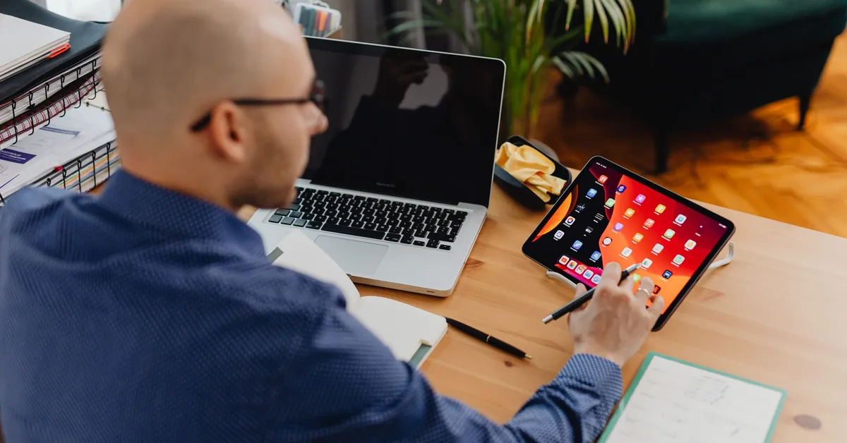 A man using a tablet and laptop at a desk in a modern office setting. a man using a digital tablet