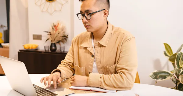 Young Asian man focused on work, using a laptop at a modern home office. a businessman using a laptop