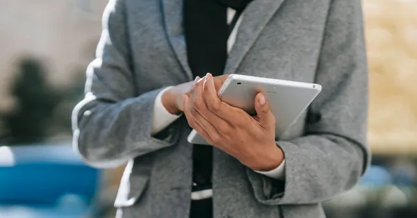 Crop unrecognizable female entrepreneur in formal outfit using tablet while standing on city street on sunny day faceless businesswoman browsing table on street