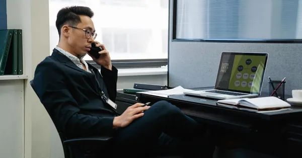 Man in a suit working in an office, talking on phone with laptop and documents. man talking on phone at work