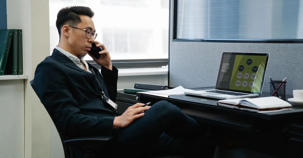 Man in a suit working in an office, talking on phone with laptop and documents. man talking on phone at work
