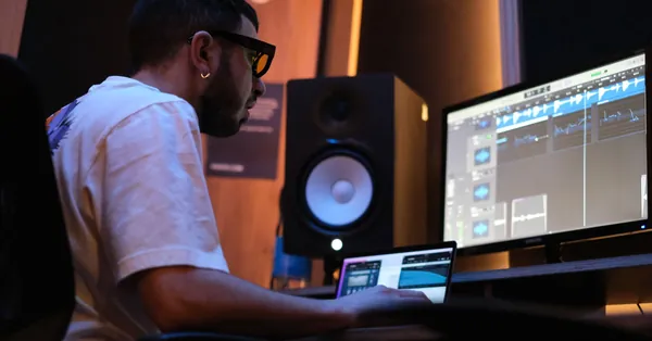 Music producer at a computer in a London studio, focusing on audio editing on multiple screens. man working in white shirt sitting in front of a monitor and speaker