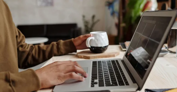 Close-up of a person using a laptop with a coffee mug on a wooden table, ideal for remote work concept. close up photo of person using gray laptop