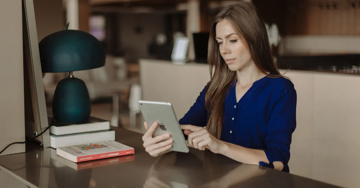 Woman reading on a tablet at a desk with books in a modern office setting. woman reading on tablet in modern office space