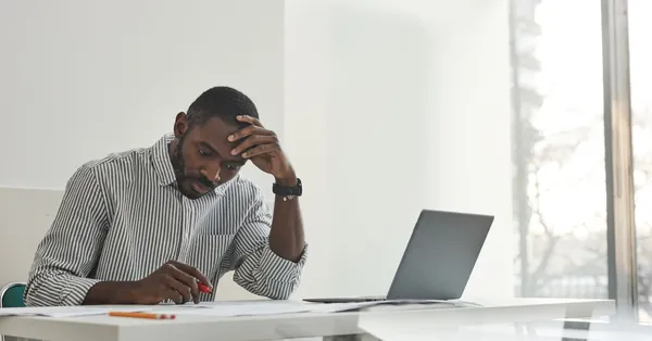 Pensive man at desk working with laptop and papers in modern office space. a man sitting while working