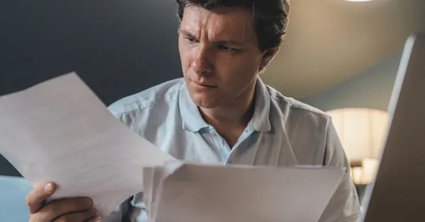 A man intently examines papers, seated indoors under warm lighting, focusing on his work. a man holding printer papers