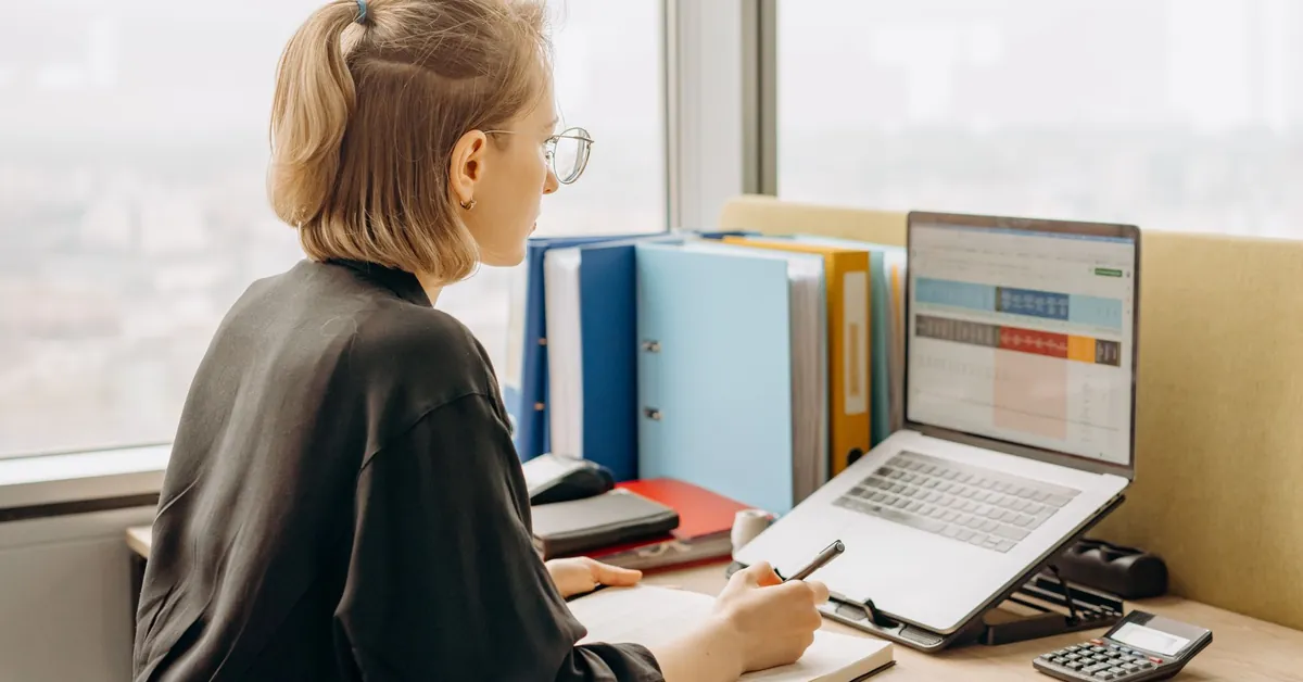 A side view of a professional woman working on a laptop with spreadsheets in a modern office. woman looking at the screen of her laptop