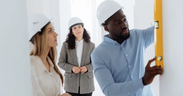 Group of diverse contractors collaborating on a construction project indoors, using a level bar. people checking a wall using a level bar