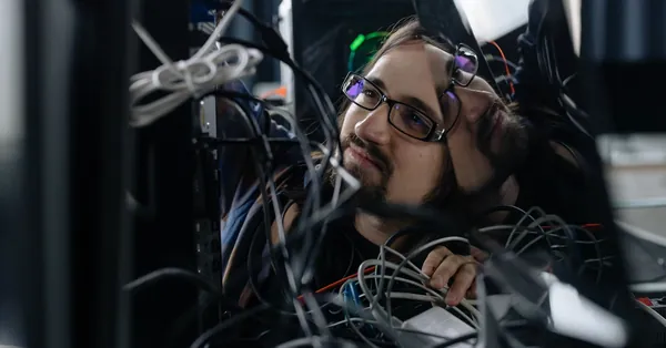 A skilled IT technician organizing tangled cables at his workstation in an office environment. employee working through the tangle of cables behind the computer