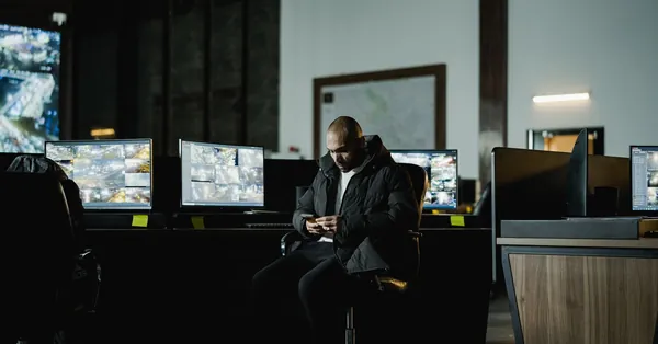 Security officer seated in a dimly lit control room, analyzing multiple surveillance screens. security officer in dark control room with monitors