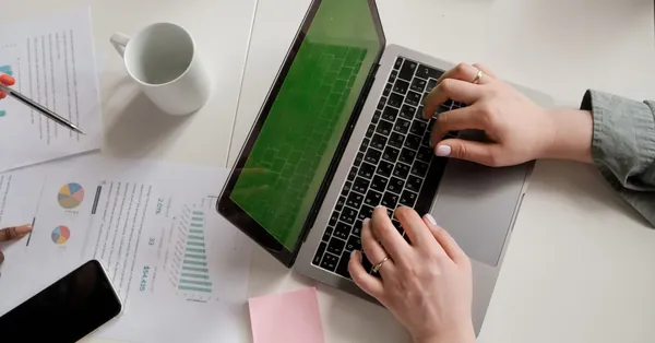 Modern office desk setup with a laptop, papers, and hands typing. a person using a laptop