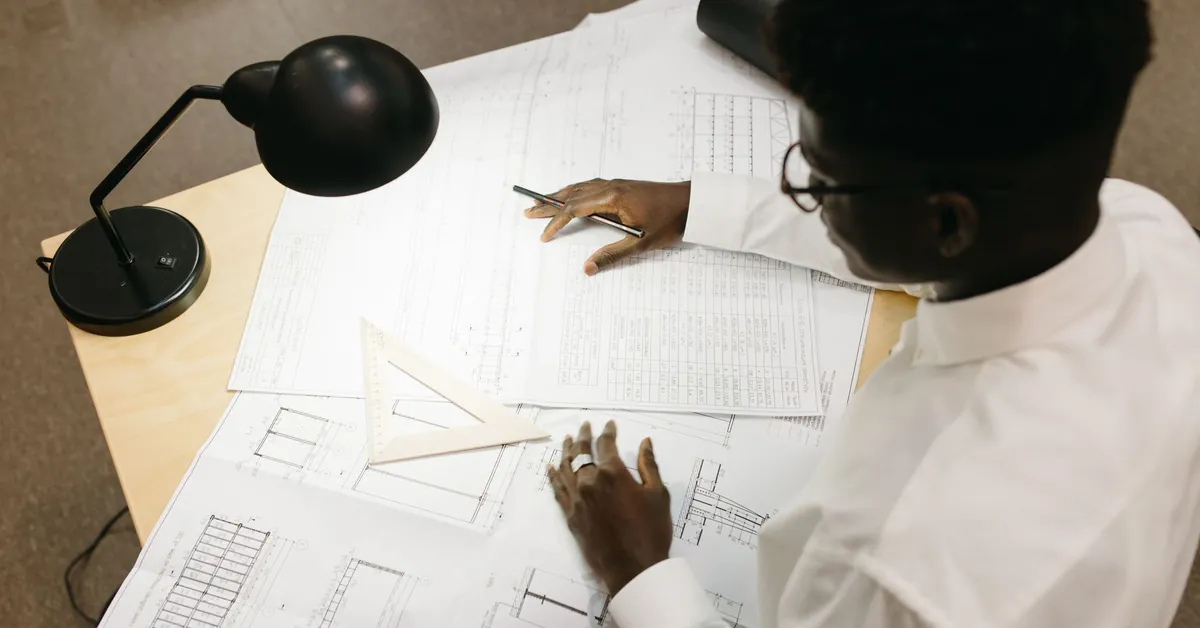 Top view of architect with afro hair working on blueprints at desk inside an office. a man sitting at the table
