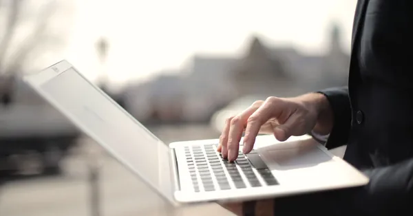 A business professional typing on a laptop in an outdoor setting, symbolizing remote work. person using macbook air