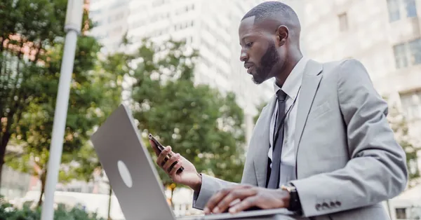 Businessman in a suit using a laptop and smartphone in an urban setting, blending technology with business. man using his laptop and a smart phone