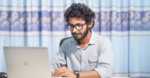A focused young man using a laptop in a well-lit room. Ideal for themes of productivity and tech. young man working on laptop in bright room