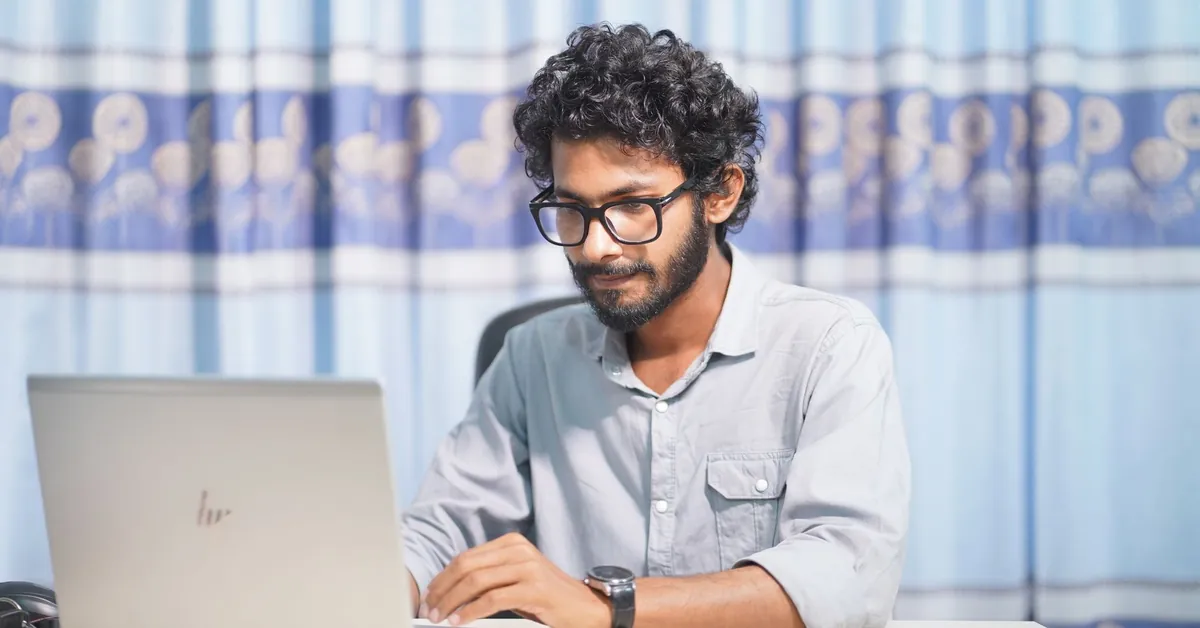 A focused young man using a laptop in a well-lit room. Ideal for themes of productivity and tech. young man working on laptop in bright room