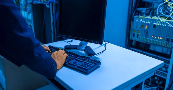 An IT professional operates a computer in a server room, managing network systems and connected devices. it technician working in data center server room