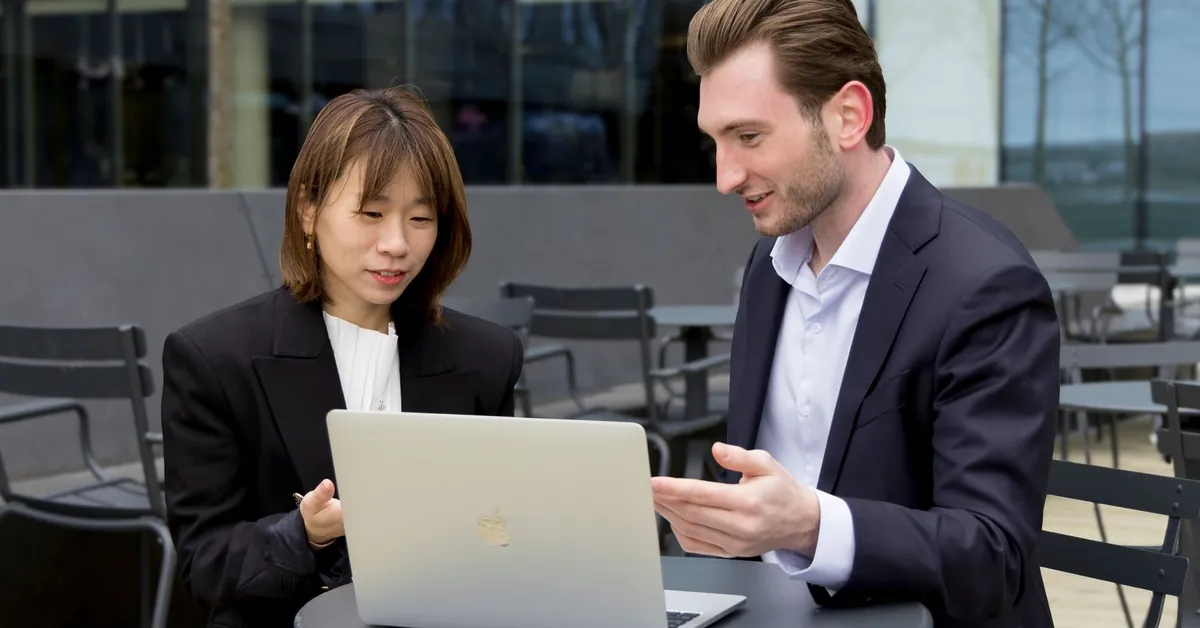Two professionals collaborating over a laptop during an outdoor business meeting. smiling businessman and businesswoman looking at a laptop and talking at a table in front of an office building