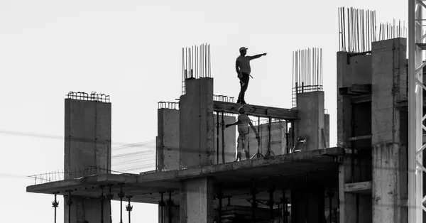 Silhouette of construction workers on a building site with one pointing towards the distance. black and white construction workers on site