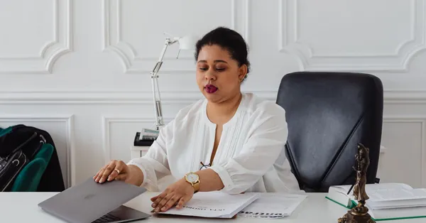 Confident businesswoman in a white blouse working at a stylish office desk with a laptop and legal documents. a woman sitting on the black leather seat at the white table with laptop
