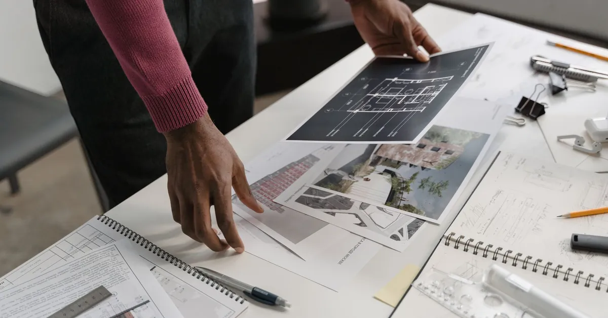 Architect evaluates blueprints on a desk, showcasing modern workspace creativity and design. person in red long sleeve shirt holding white printer paper